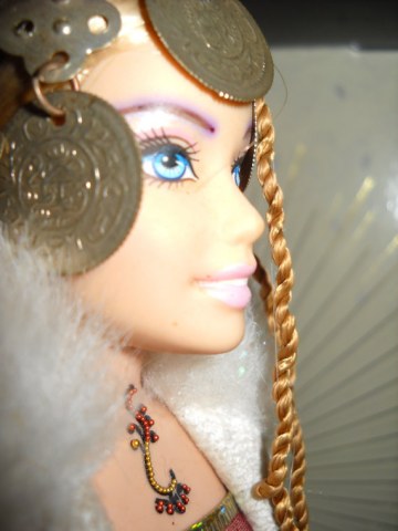 Azah wears a "Turkish Coat" of white with silver trim. Her dance attire is a band of ribbon top and a wrap skirt. She looks like a queen with her regal headress and fur neck collar. She also has some bindi adornment, and is naturally constructed of upcycled materials from dancers and barbies. 